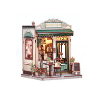 A miniature wooden model of a cozy cafe shop named 'Sunny Cafe', featuring green awnings, warm yellow interior lighting, detailed furniture, and small potted plants, set against a plain white background.