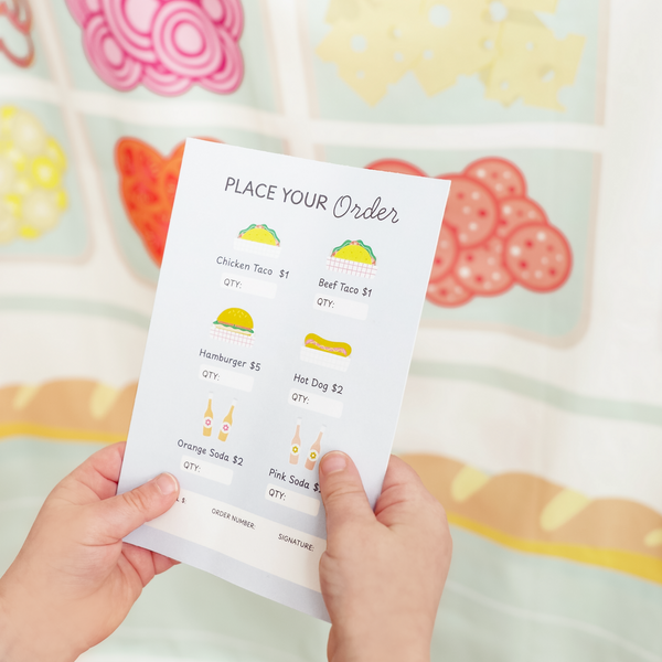 Children's play menu with food items and prices held by hands against a colorful background