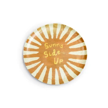 A round plate featuring a retro sunburst design in orange and cream, with the text 'Sunny Side Up' printed in yellow in the center, set against a plain white background.