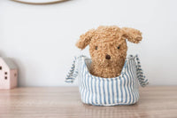 Stuffed dog toy in a blue and white striped bag on a wooden surface with a neutral background