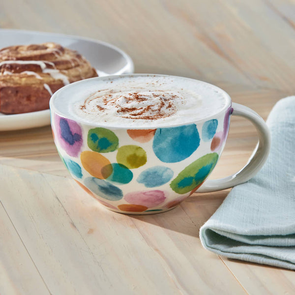 Colorful mug with polka dot pattern containing a hot beverage on a wooden surface.
