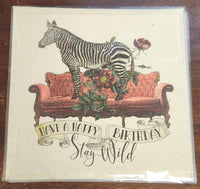 Birthday card with a zebra on a couch and floral decorations, featuring the text 'Have a Happy Birthday Stay Wild'.