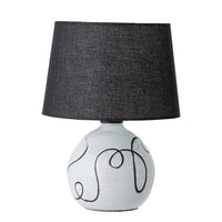 A table lamp with a white base and black swirly details, topped with a black linen shade.