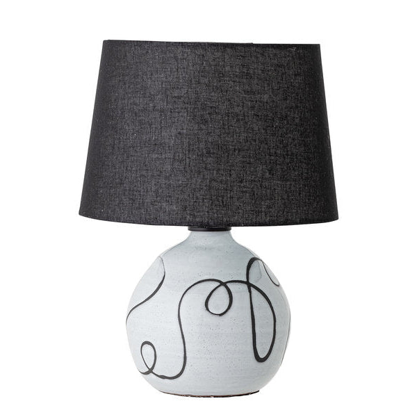 A table lamp with a white base and black swirly details, topped with a black linen shade.